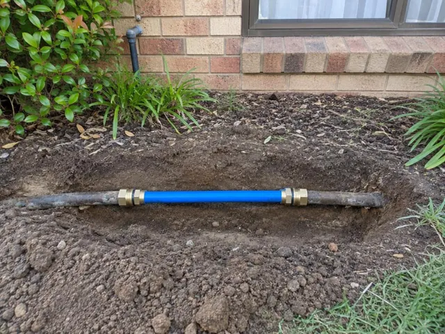 Repaired water pipe section in a garden trench beside a brick house in The Ponds