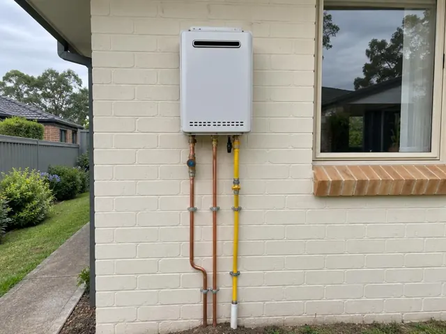 Wall-mounted hot water unit with copper and gas pipes on a brick exterior wall near a window in Beaumont Hills