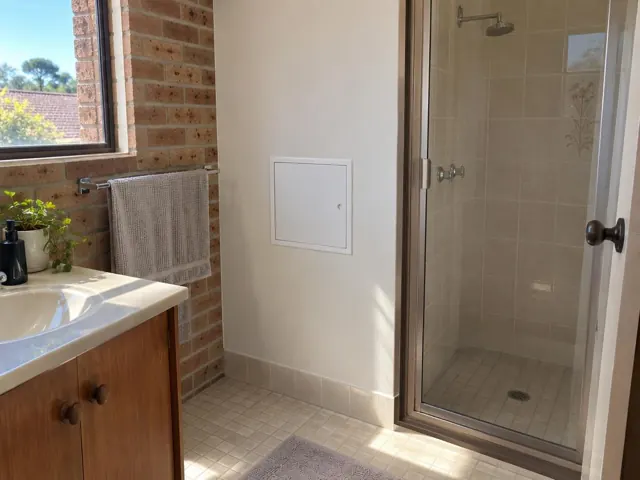 Bathroom wall with a small access panel beside a shower and vanity in Beaumont Hills